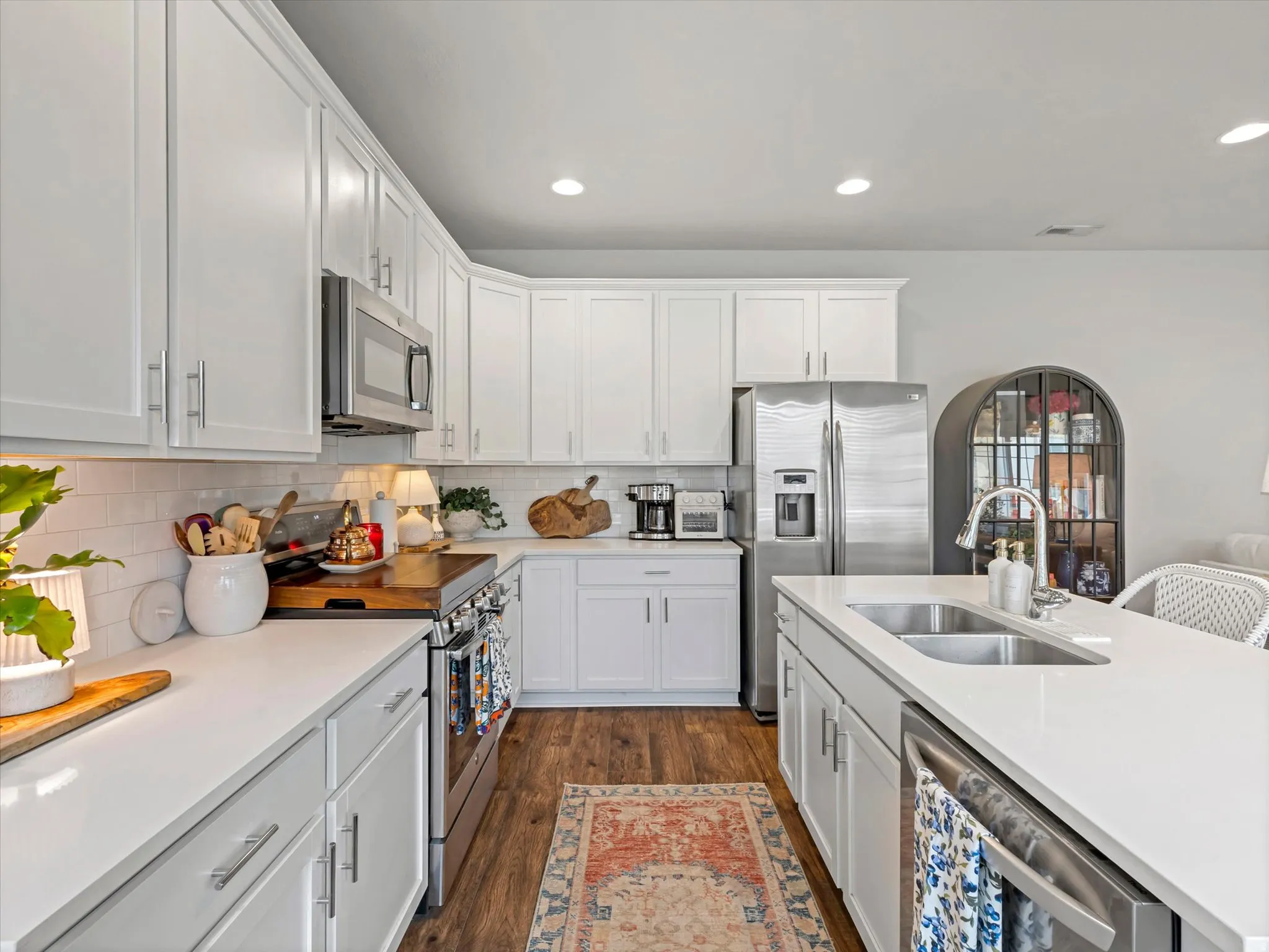 White shaker-style cabinetry, stainless steel appliances, white subway tile backsplash, white countertops, and wood-finish flooring