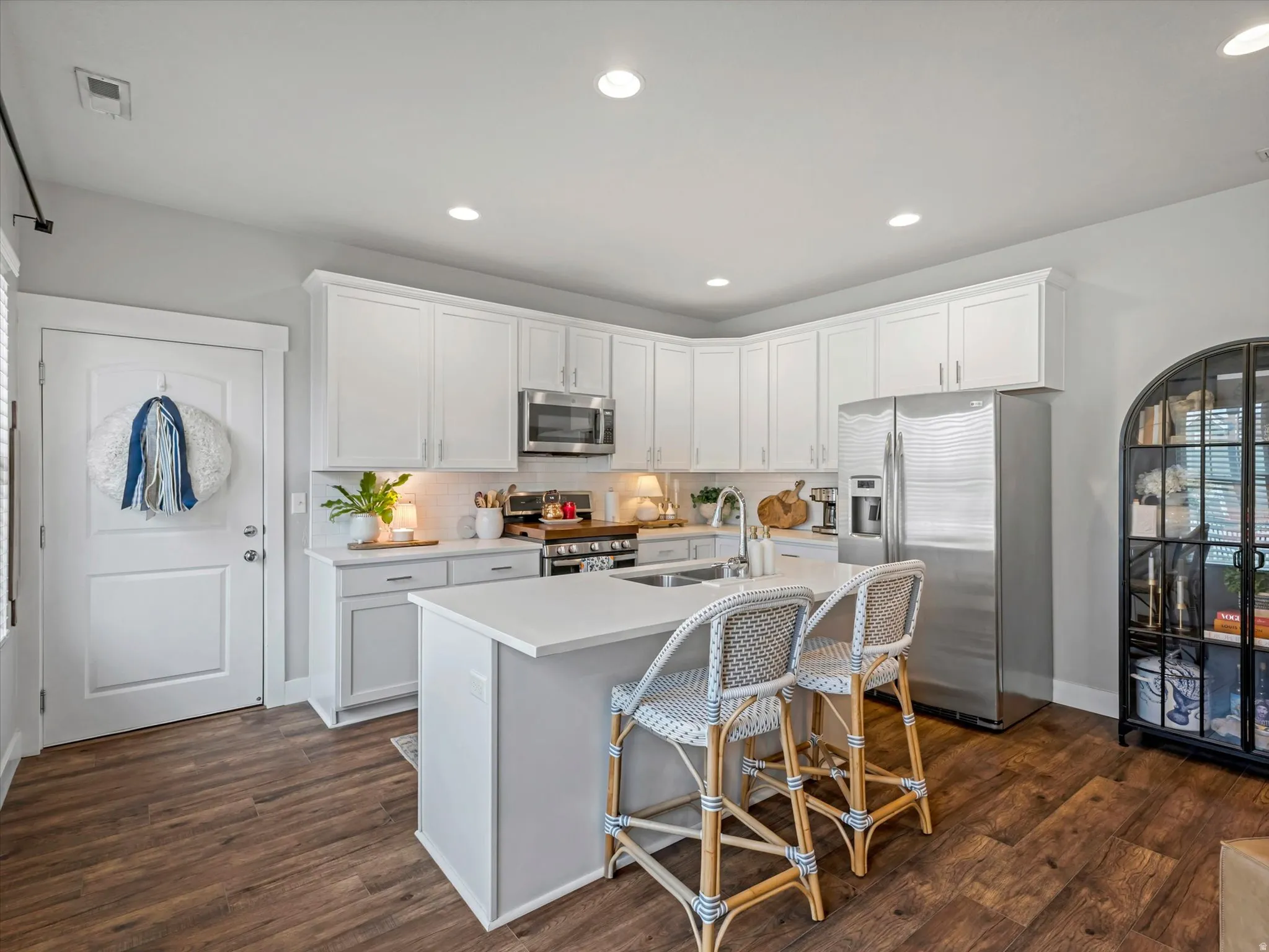 Kitchen featuring white shaker cabinetry, stainless steel appliances, a center island with countertop seating, wood-finish flooring, and recessed lighting