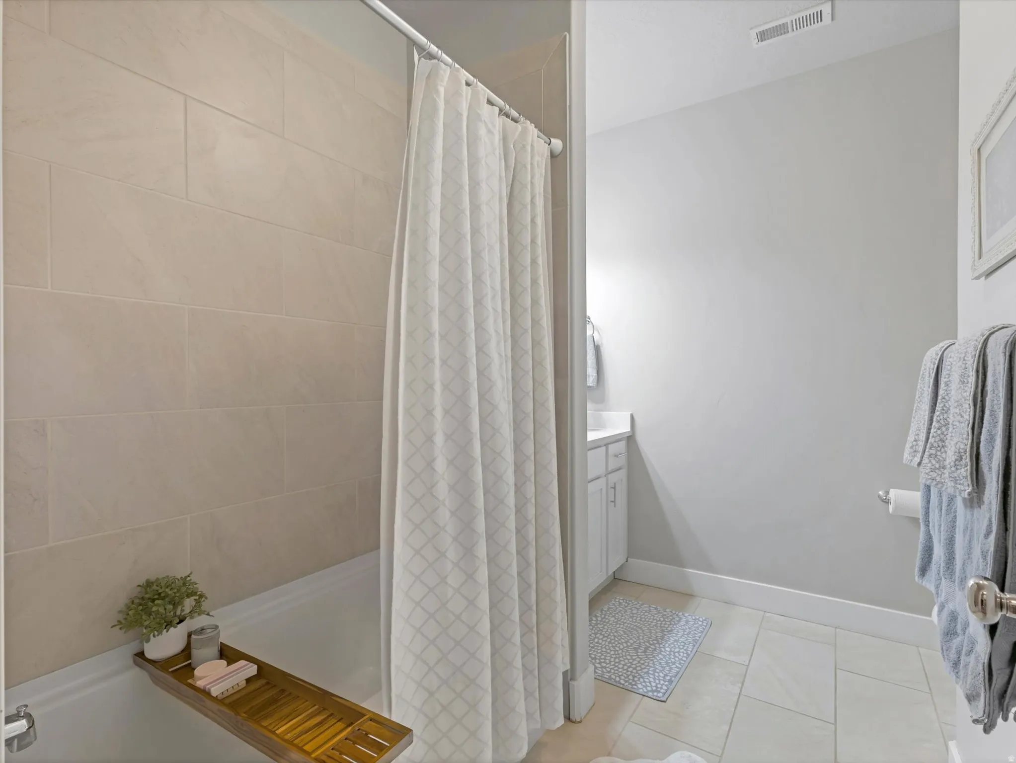 White bathtub with beige tile surround, light gray walls, and white cabinetry