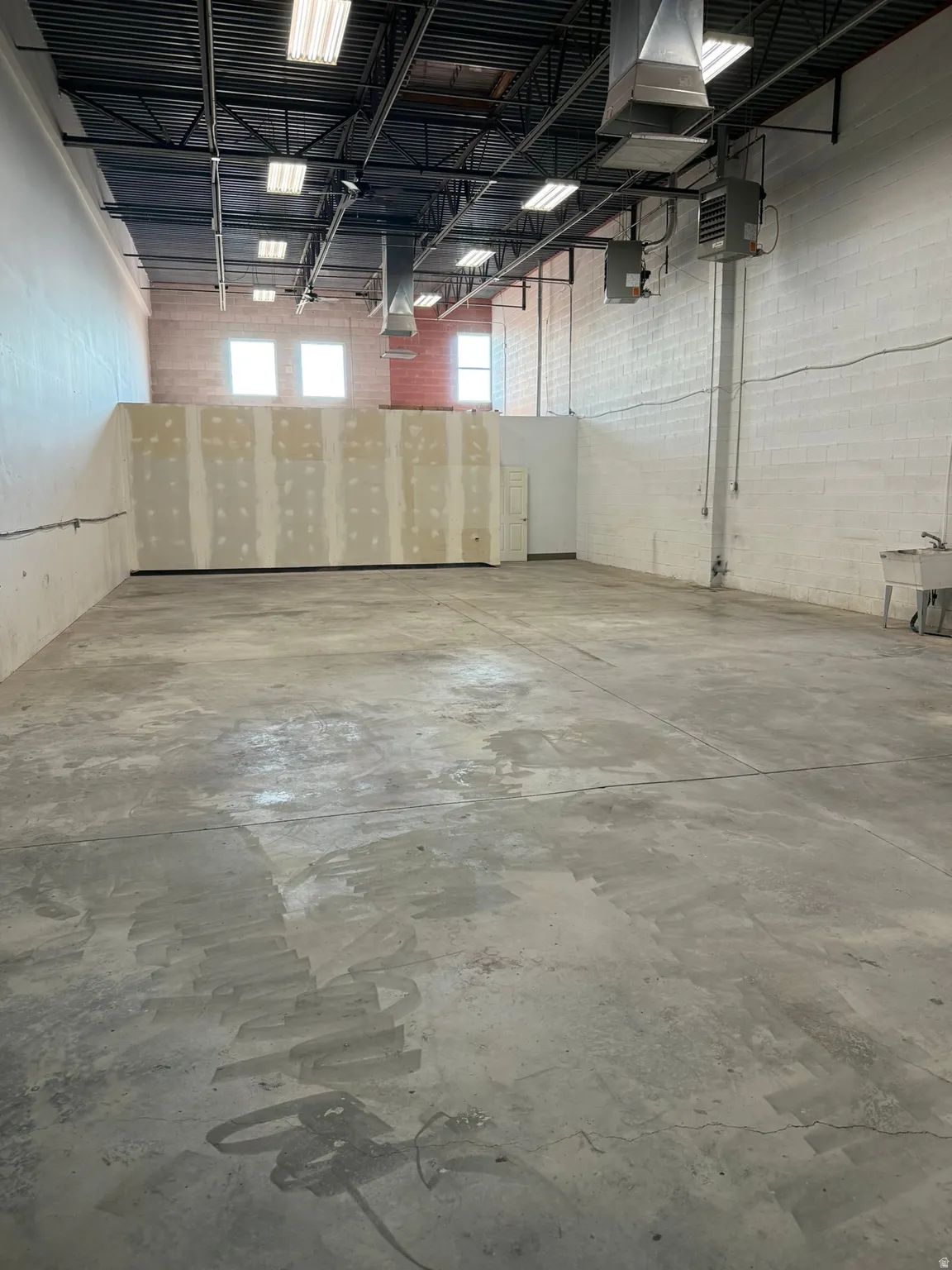 Open floor plan featuring concrete flooring, exposed ceiling with ductwork, multiple windows, and a utility sink