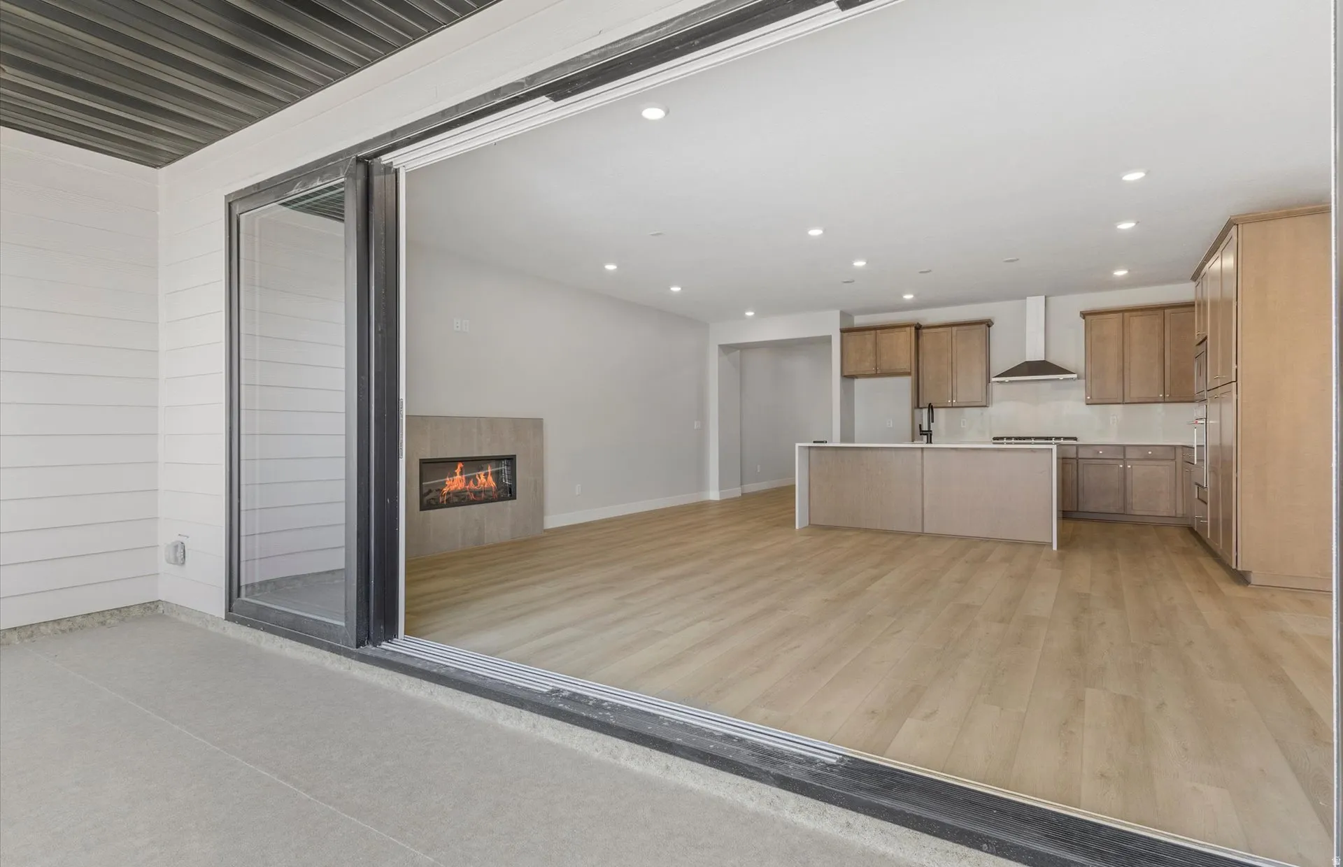 Expansive sliding glass doors open to a modern kitchen featuring wood-finish cabinetry, a large island, stainless steel appliances, and a tiled backsplash