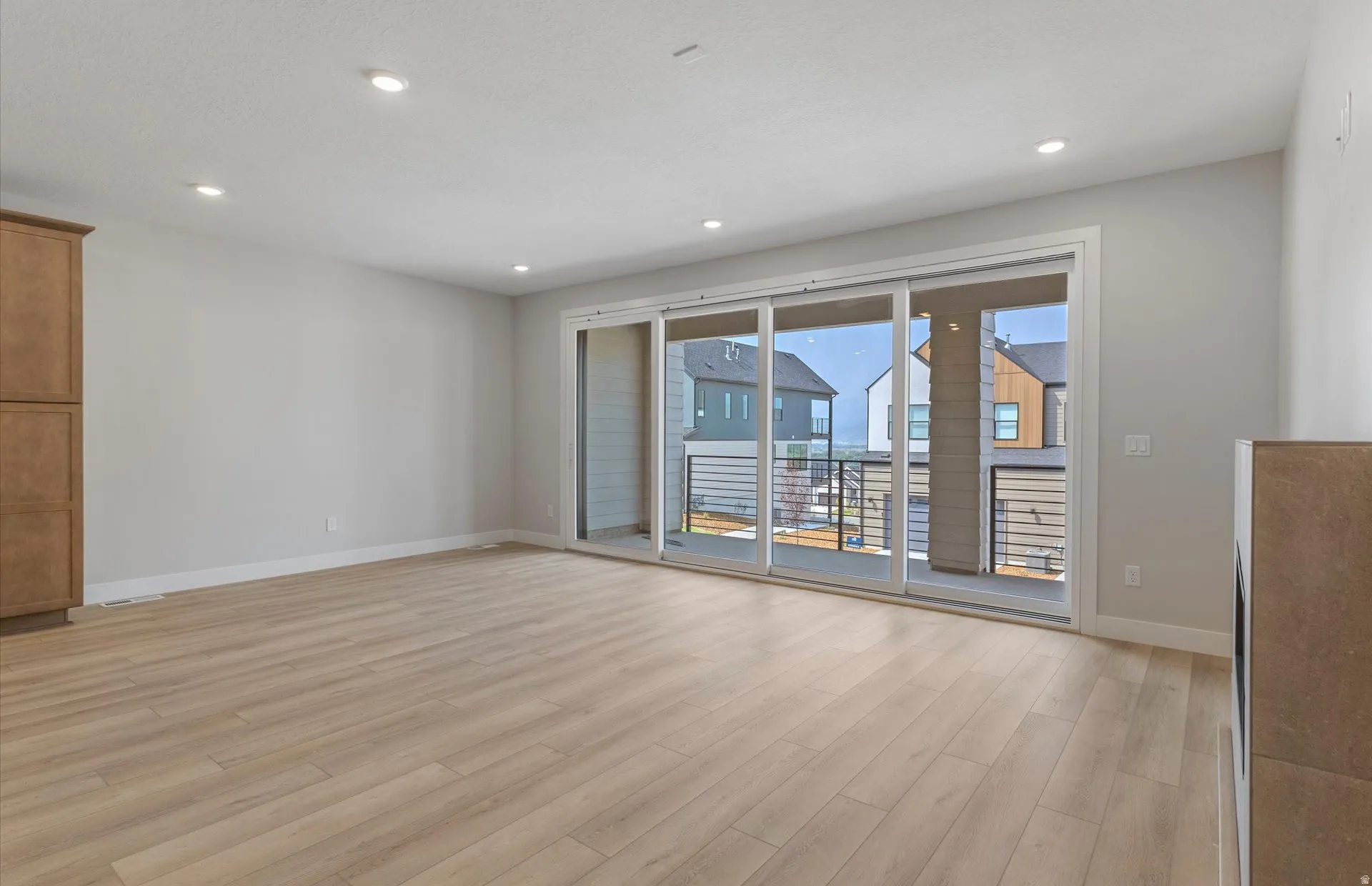Recessed lighting, wood-finish flooring, built-in cabinetry, and a full-light sliding glass door to an outdoor balcony with metal railings
