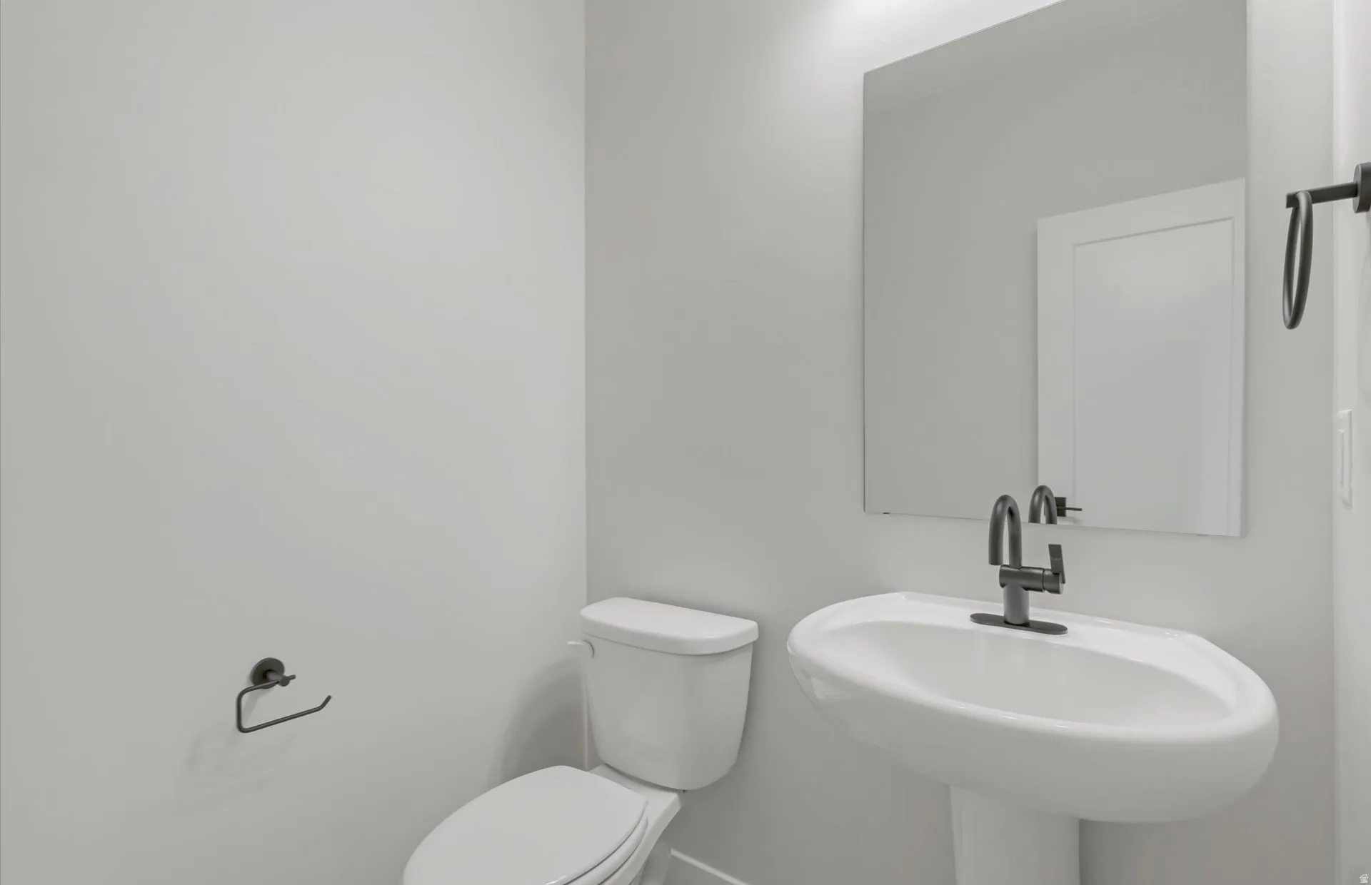 Pedestal sink with a dark-finish faucet, rectangular wall mirror, and modern toilet