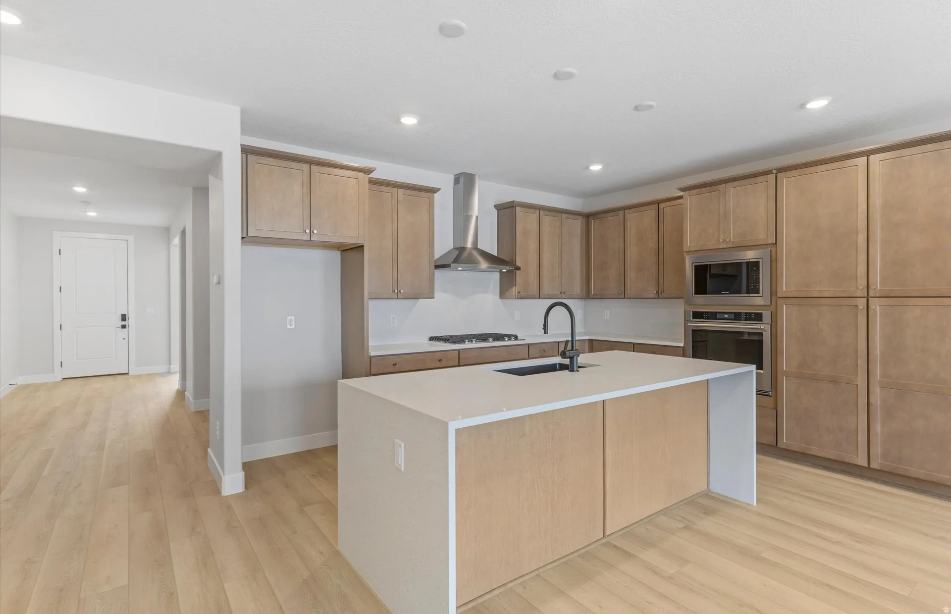 Kitchen featuring light wood-finish cabinetry, stainless steel appliances, a center island with an integrated sink, and recessed lighting