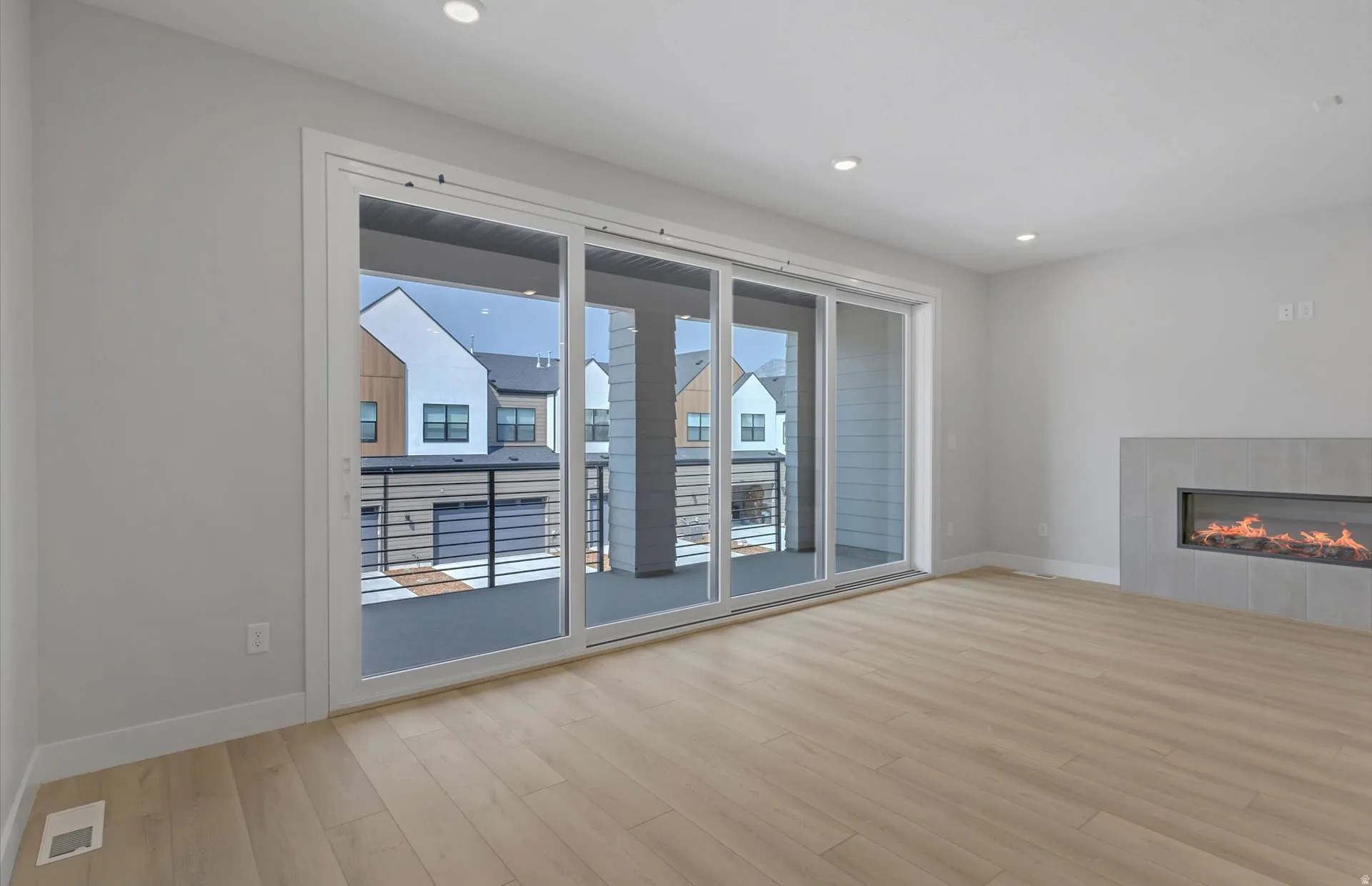 Spacious room featuring wood-finish flooring, recessed lighting, and a modern linear fireplace with a light-toned surround