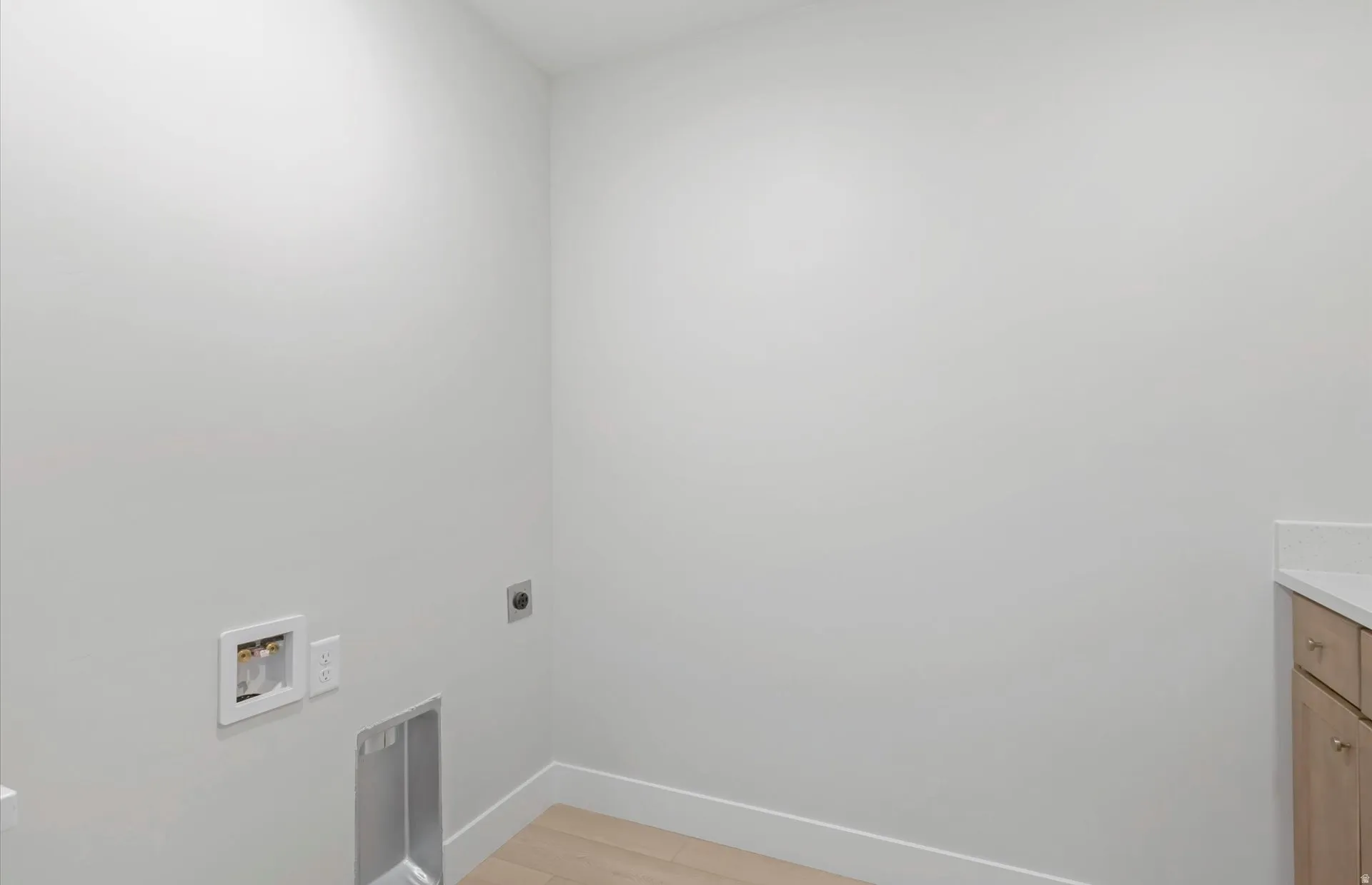 Dedicated utility space featuring light wood-finish flooring, light-toned walls, and a built-in counter with cabinetry