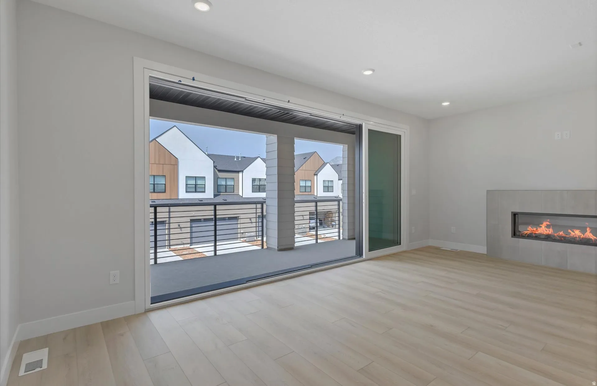 Light wood-finish flooring, recessed lighting, and a modern linear fireplace with a tile surround