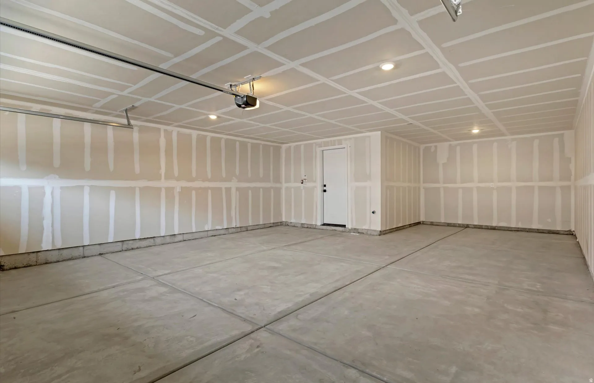 Spacious garage with exposed drywall, concrete flooring, and an automatic garage door opener