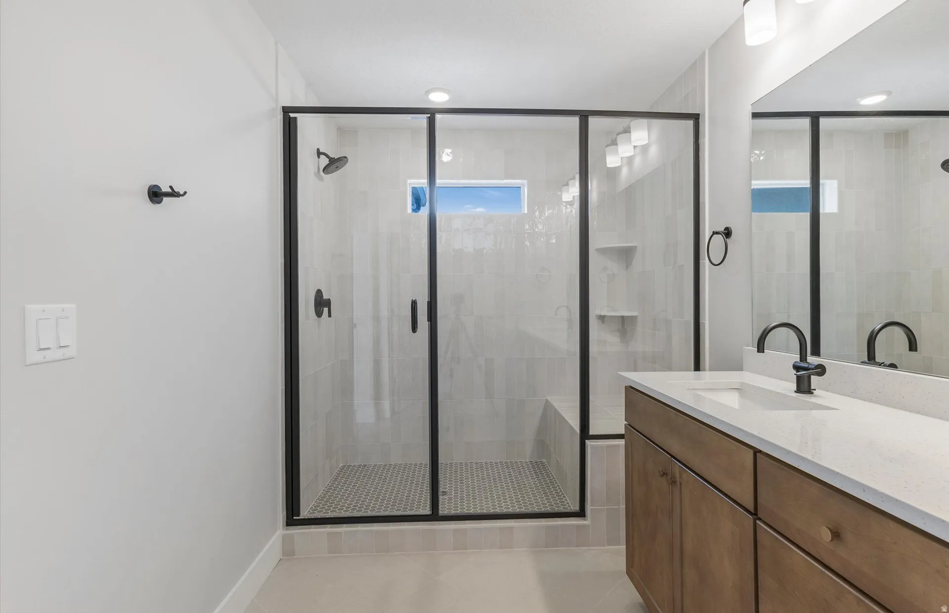 Walk-in shower with black-framed glass enclosure, tiled walls, and built-in bench