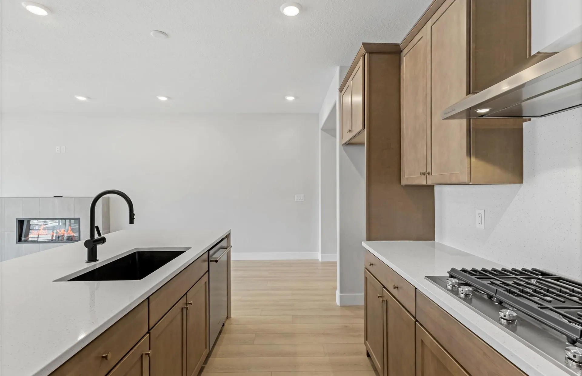 Kitchen featuring light wood-finish flooring, white countertops, built-in cooktop, stainless steel range hood, and matte black sink