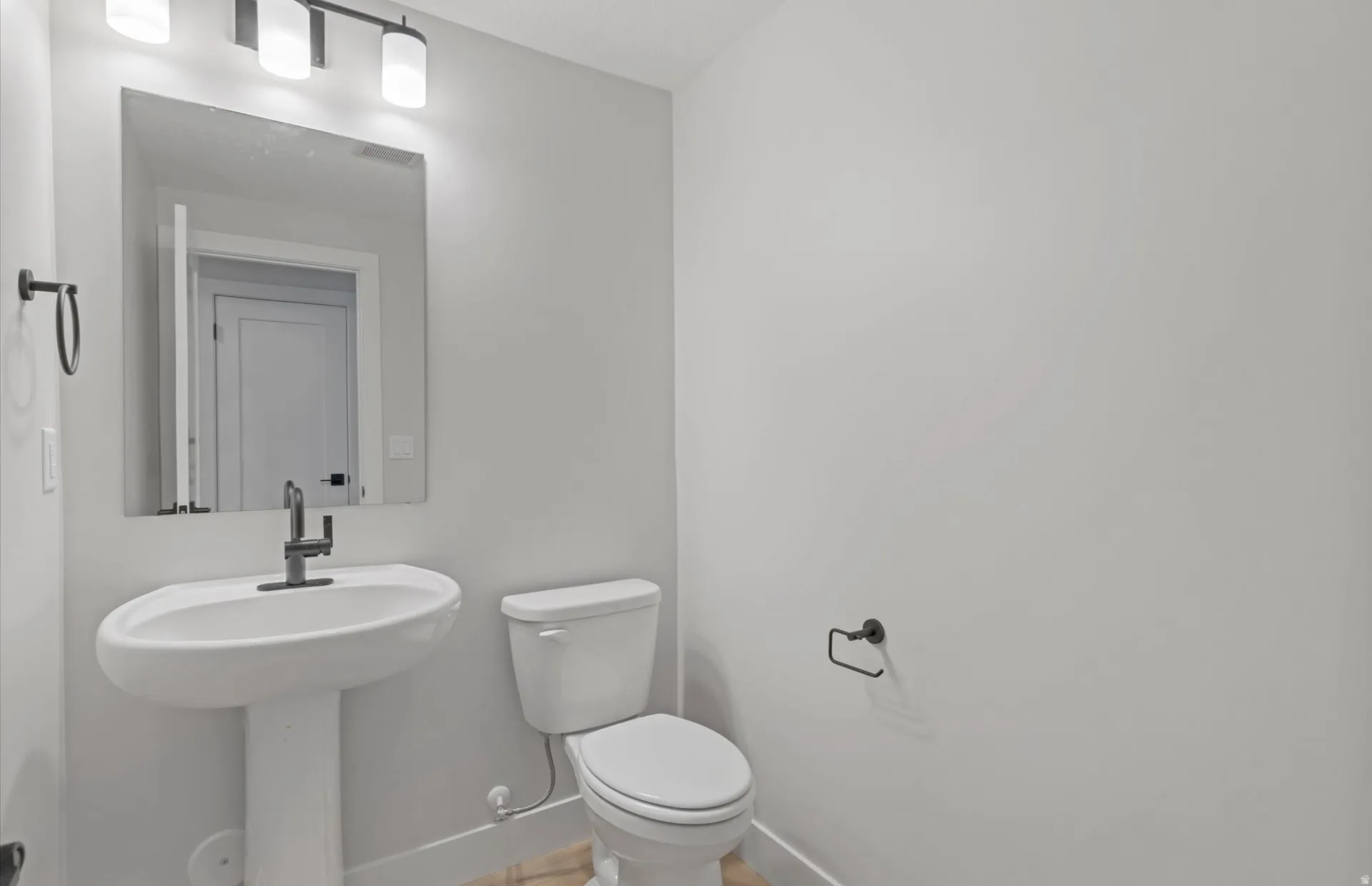 Pedestal sink with a matte black faucet, wall-mounted mirror, and contemporary light fixture