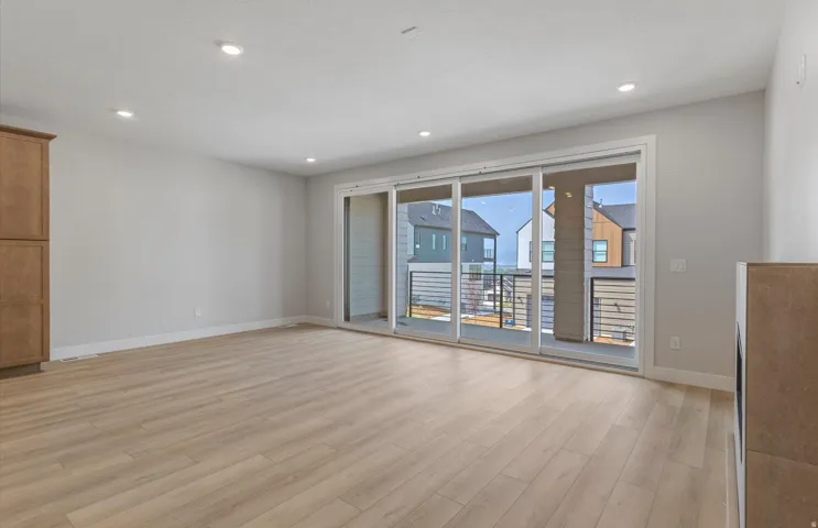 Recessed lighting, wood-finish flooring, built-in cabinetry, and a full-light sliding glass door to an outdoor balcony with metal railings