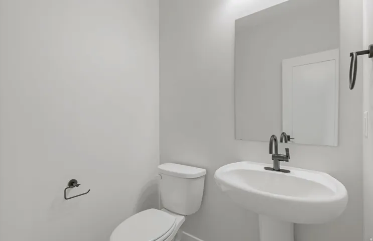 Pedestal sink with a dark-finish faucet, rectangular wall mirror, and modern toilet