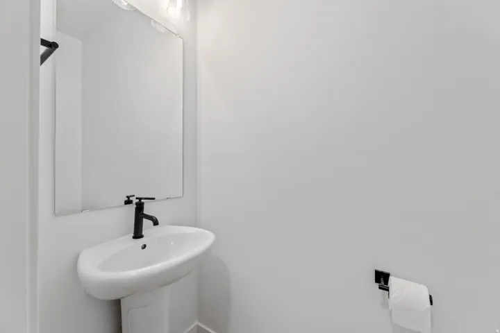 Pedestal sink with a matte black faucet, wall-mounted mirror, and overhead vanity lighting