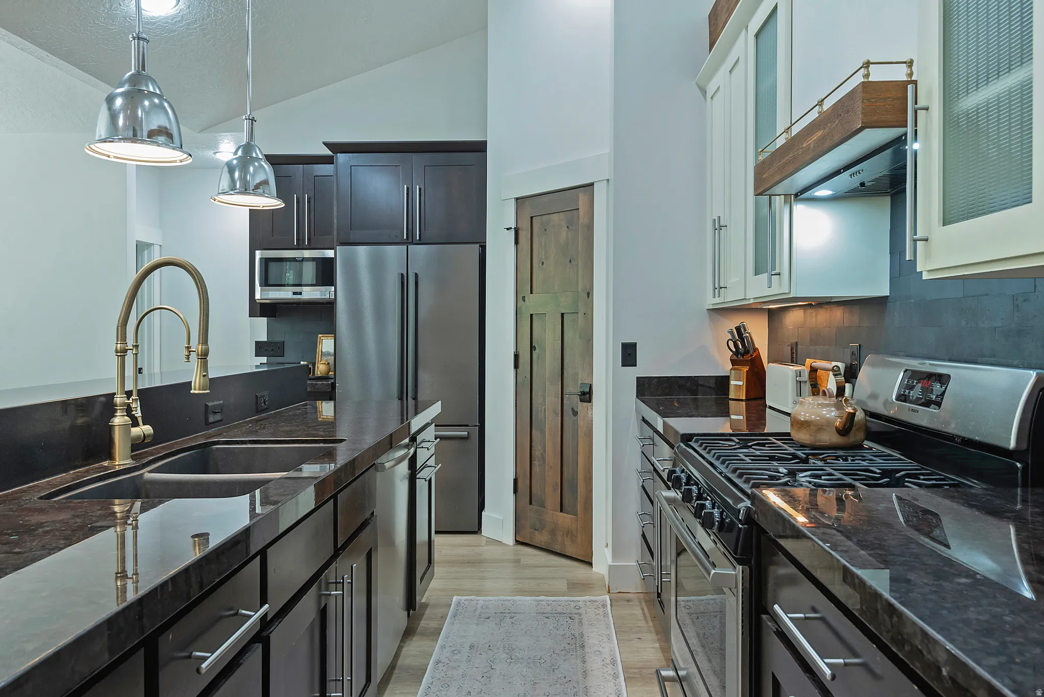 Stainless steel appliances, dark stone countertops, wood-finish flooring, recessed lighting, and a vaulted ceiling