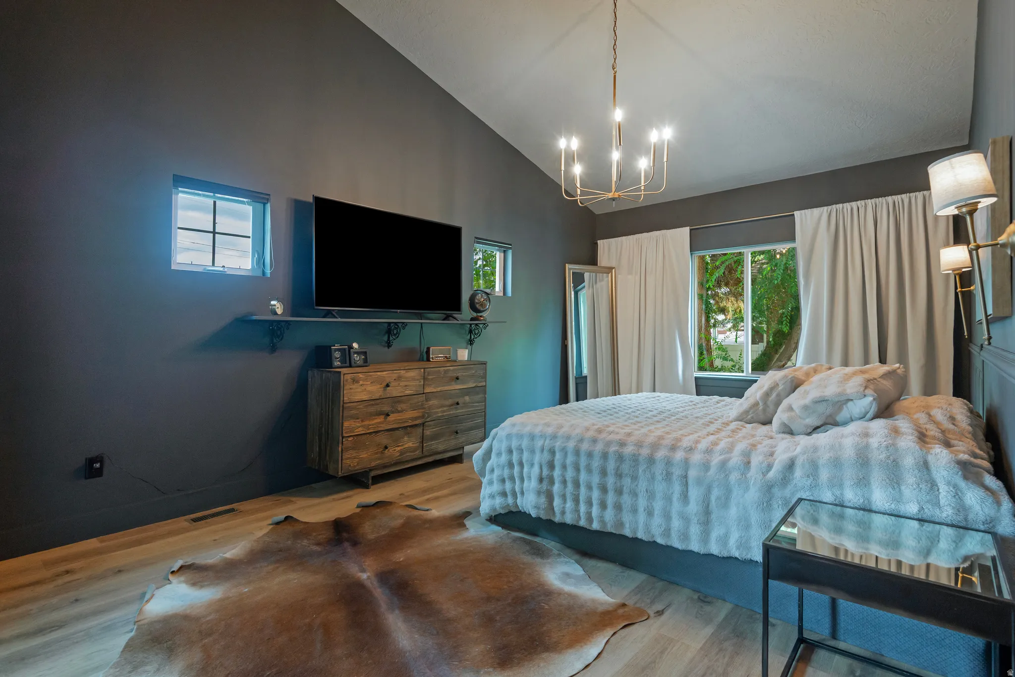 Vaulted ceiling with a chandelier, wood-finish flooring, and multiple windows