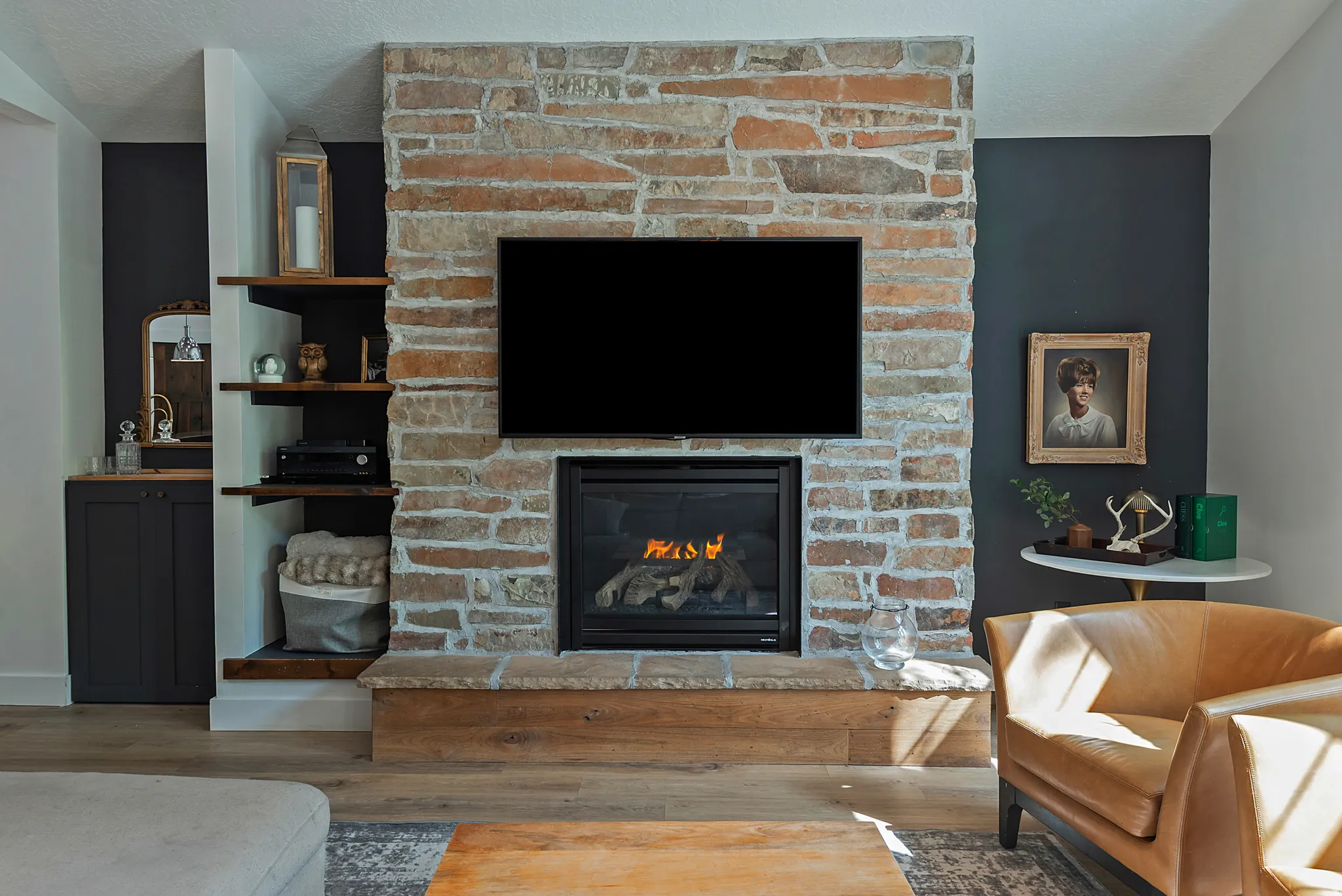 Striking focal point featuring a substantial brick fireplace with gas insert, mounted flat-screen television, and custom built-in shelving with dark cabinetry flanking either side