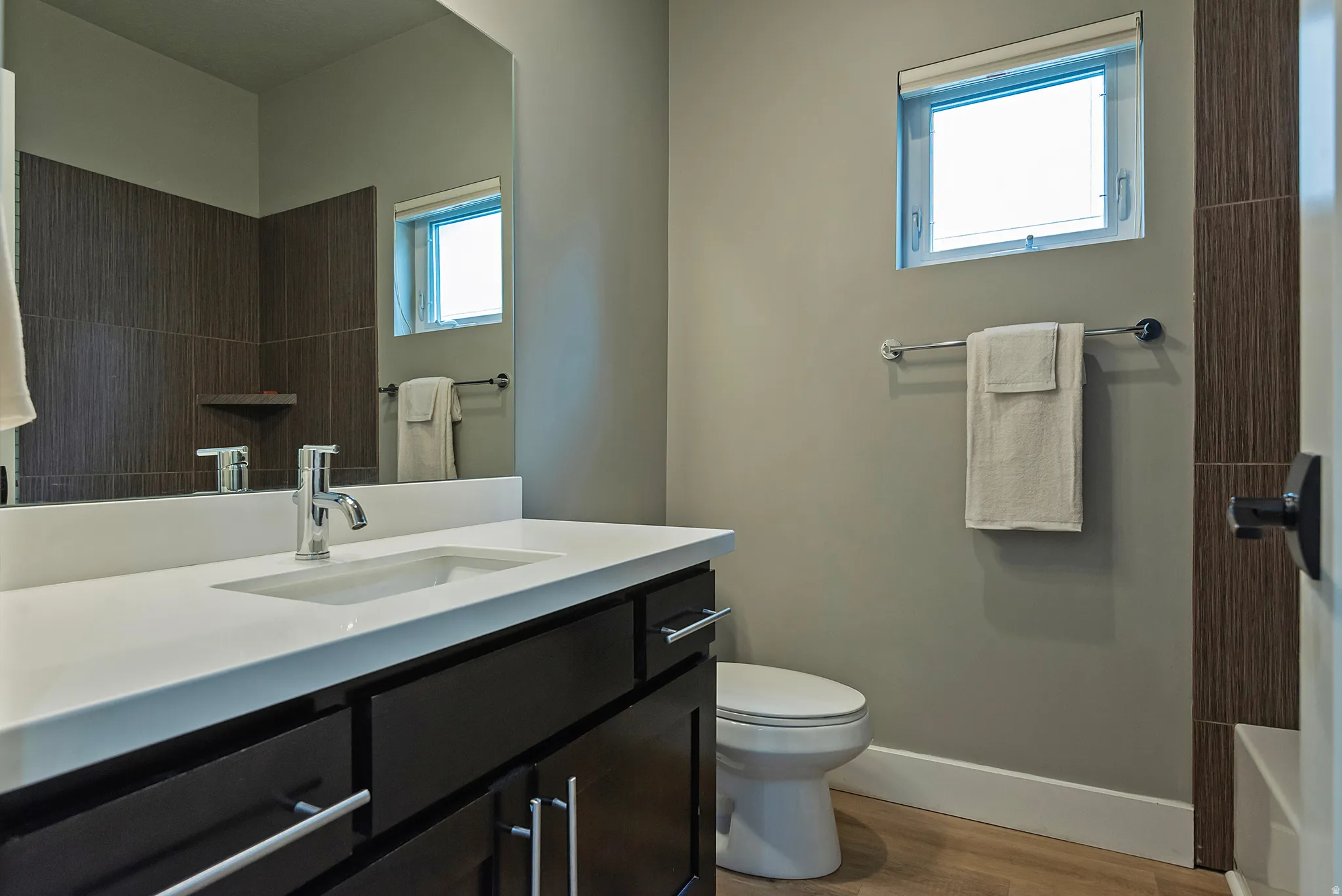 Bathroom featuring a dark wood-finish vanity with a white countertop, an integrated rectangular sink, a chrome faucet, and a large mirror
