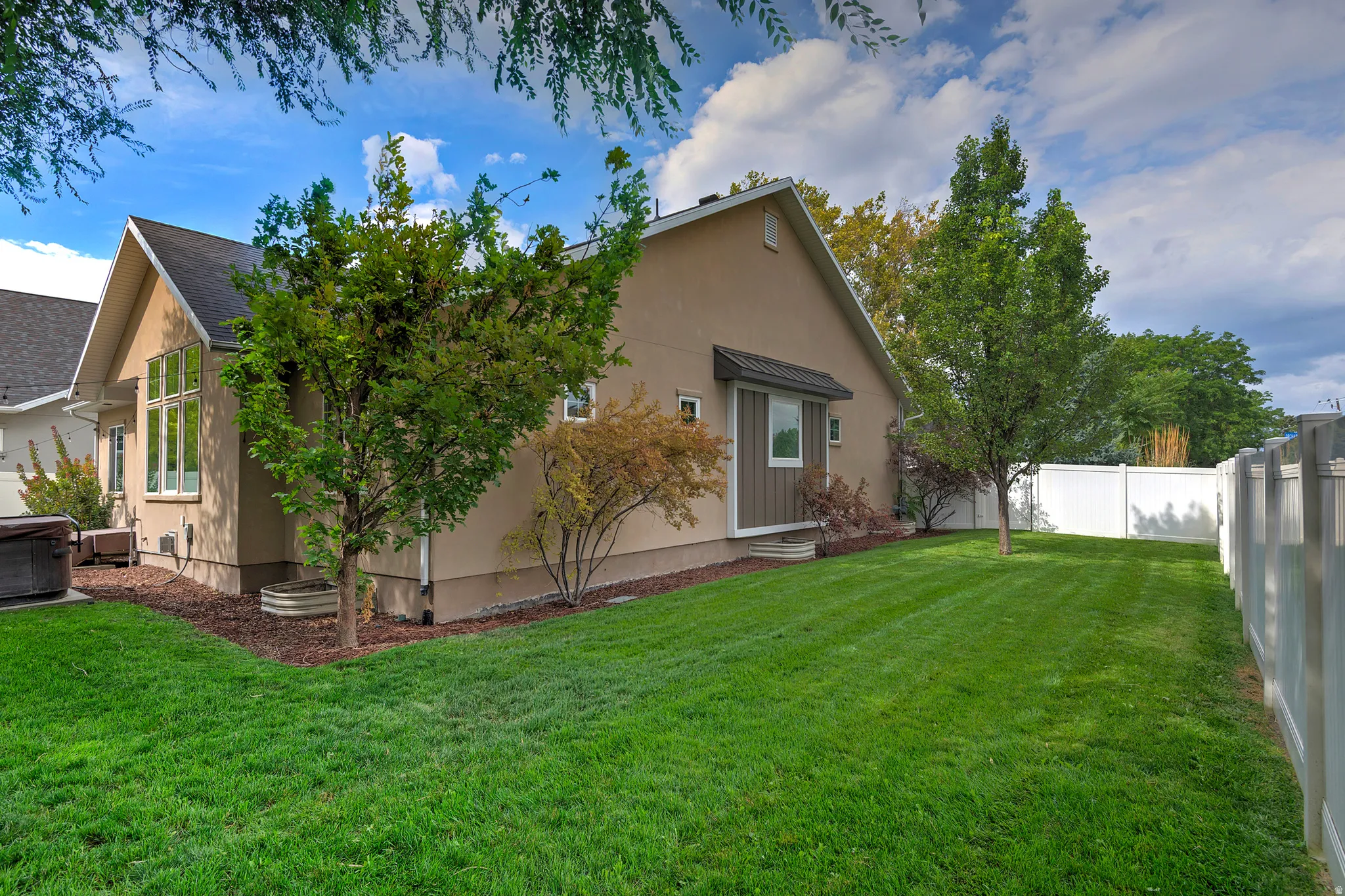 Spacious backyard with lush, manicured lawn and mature landscaping, complemented by white vinyl fencing and mature trees providing natural screening