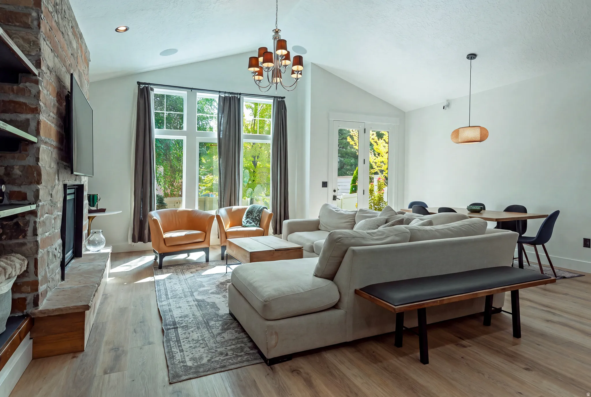 Expansive open-concept living space with soaring vaulted ceilings, large multi-pane windows flooding the room with natural light, and wide-plank wood-finish flooring throughout