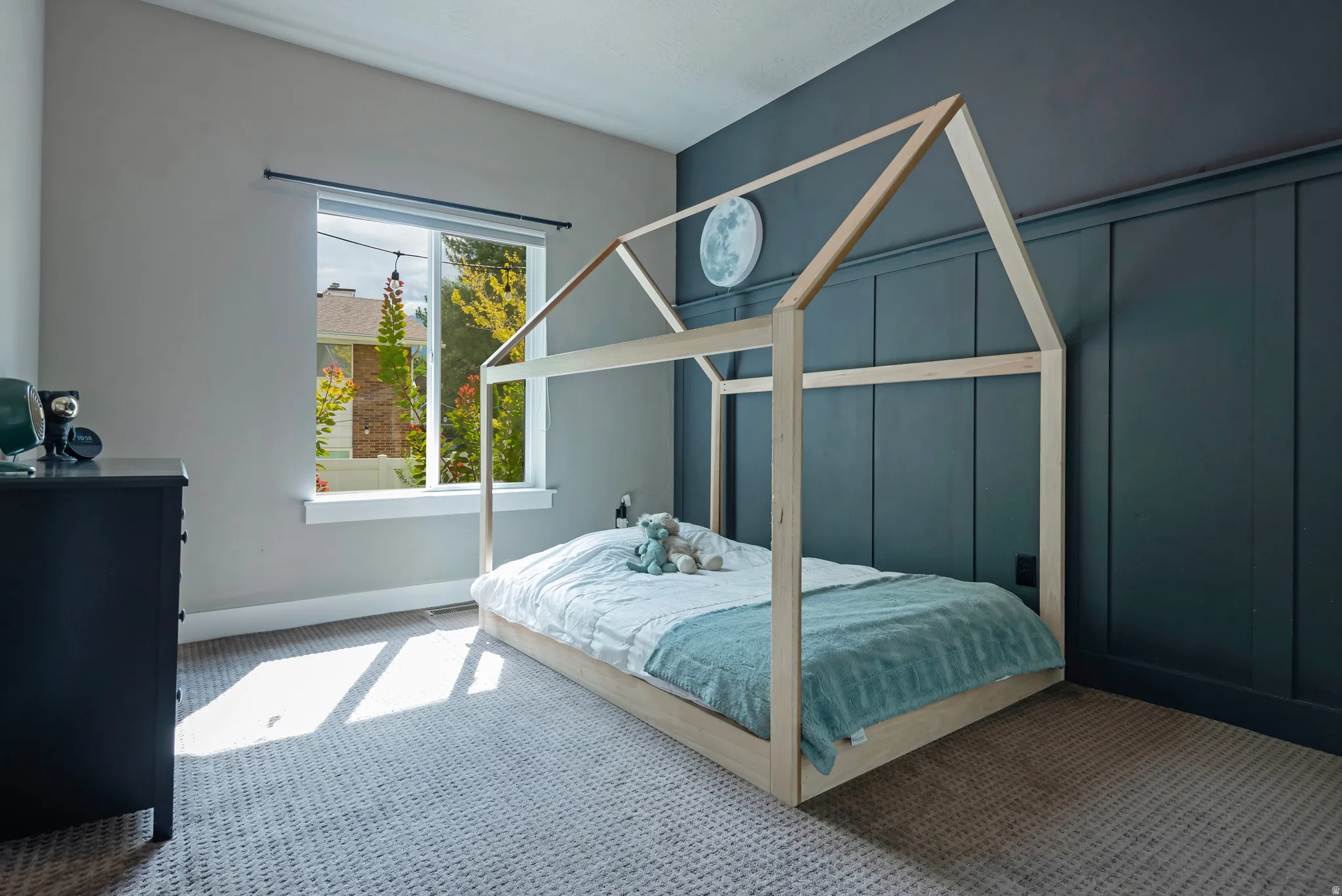 Bright bedroom featuring a wood-frame canopy bed, soft blue bedding, and natural light from a multi-pane window