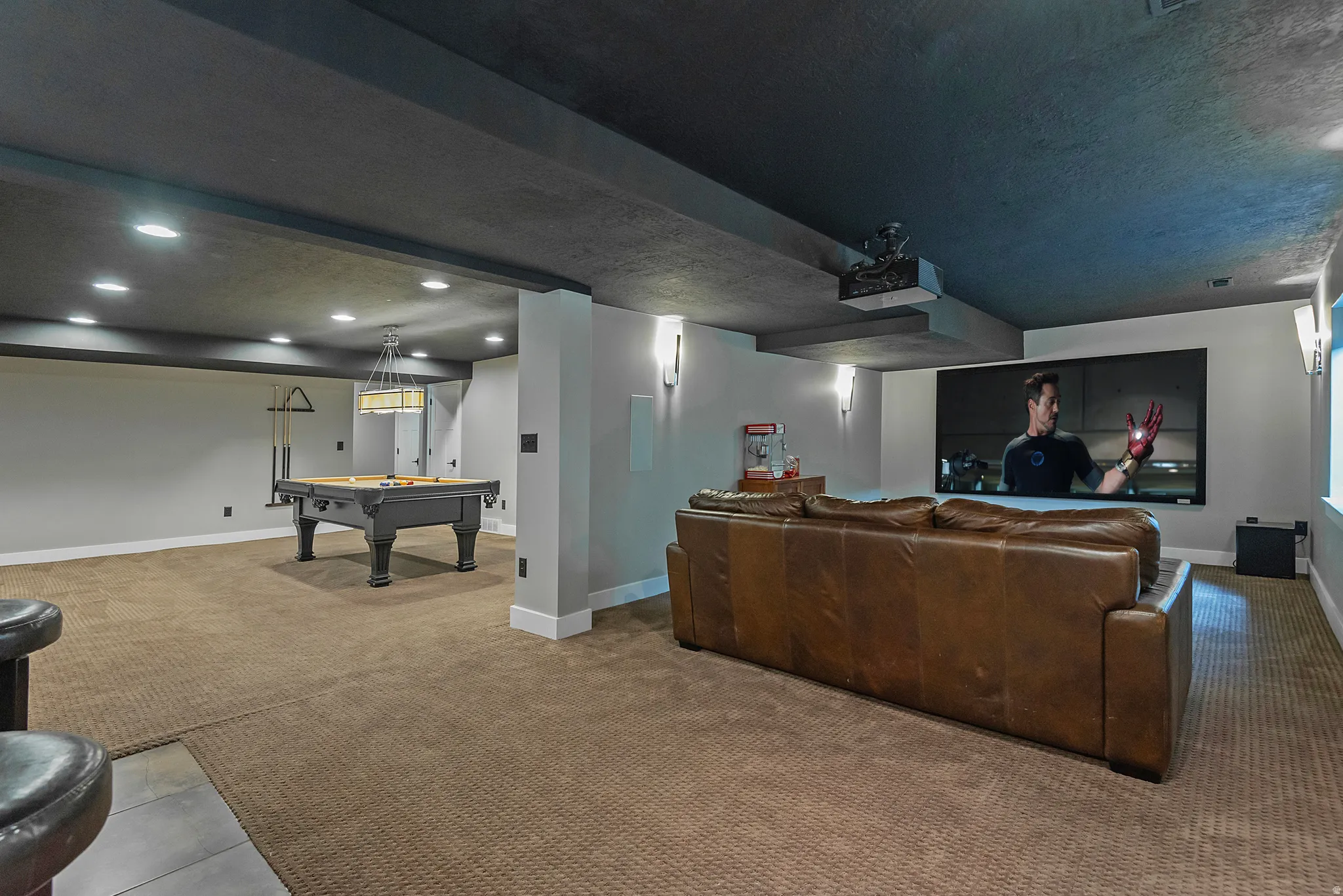 Expansive recreation room featuring engineered wood-finish flooring, recessed ceiling lighting, and a wood-finish bar with integrated storage