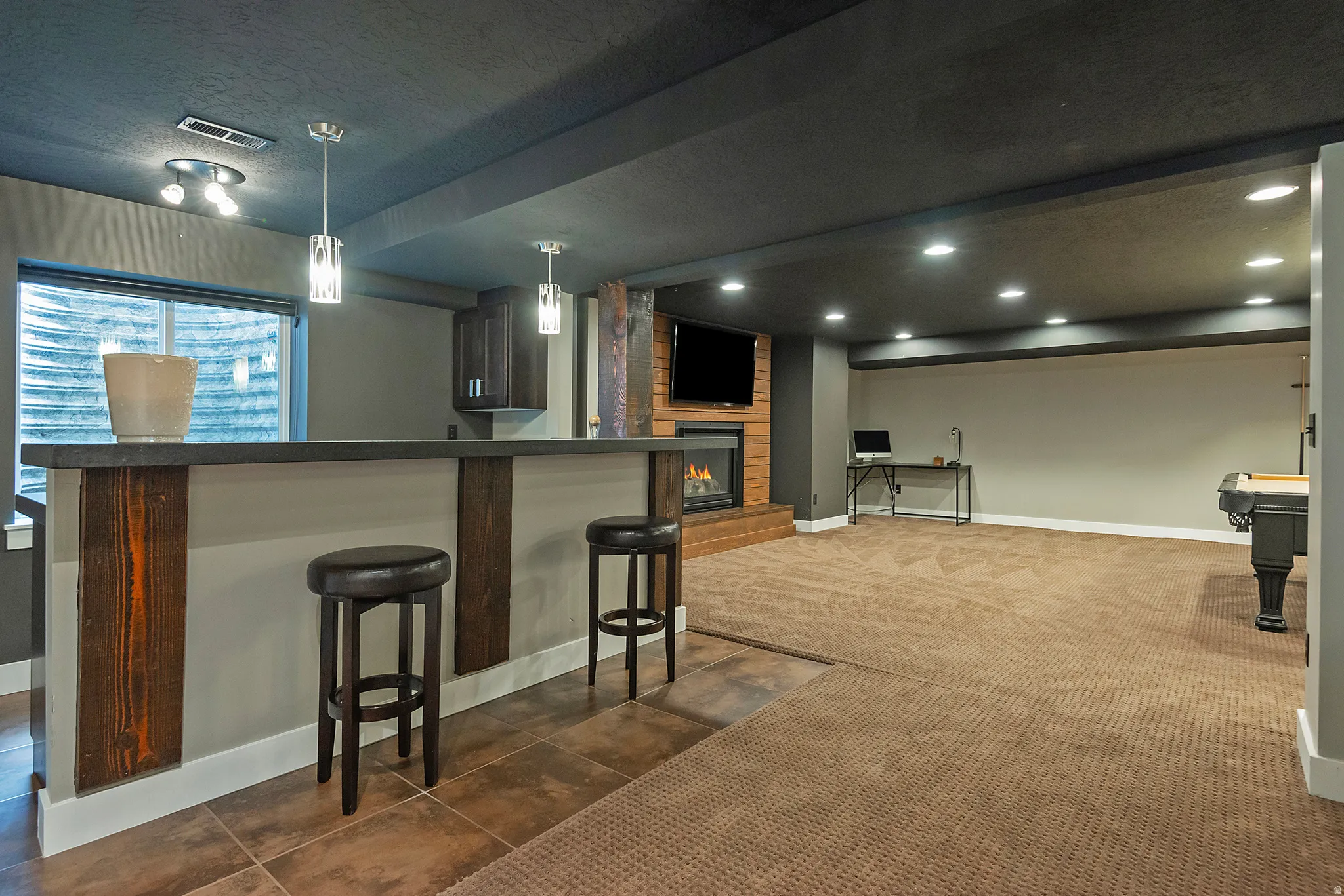 Finished lower level featuring a built-in wet bar with pendant lighting, a fireplace with a wood-look surround, recessed lighting, and a window well with natural light