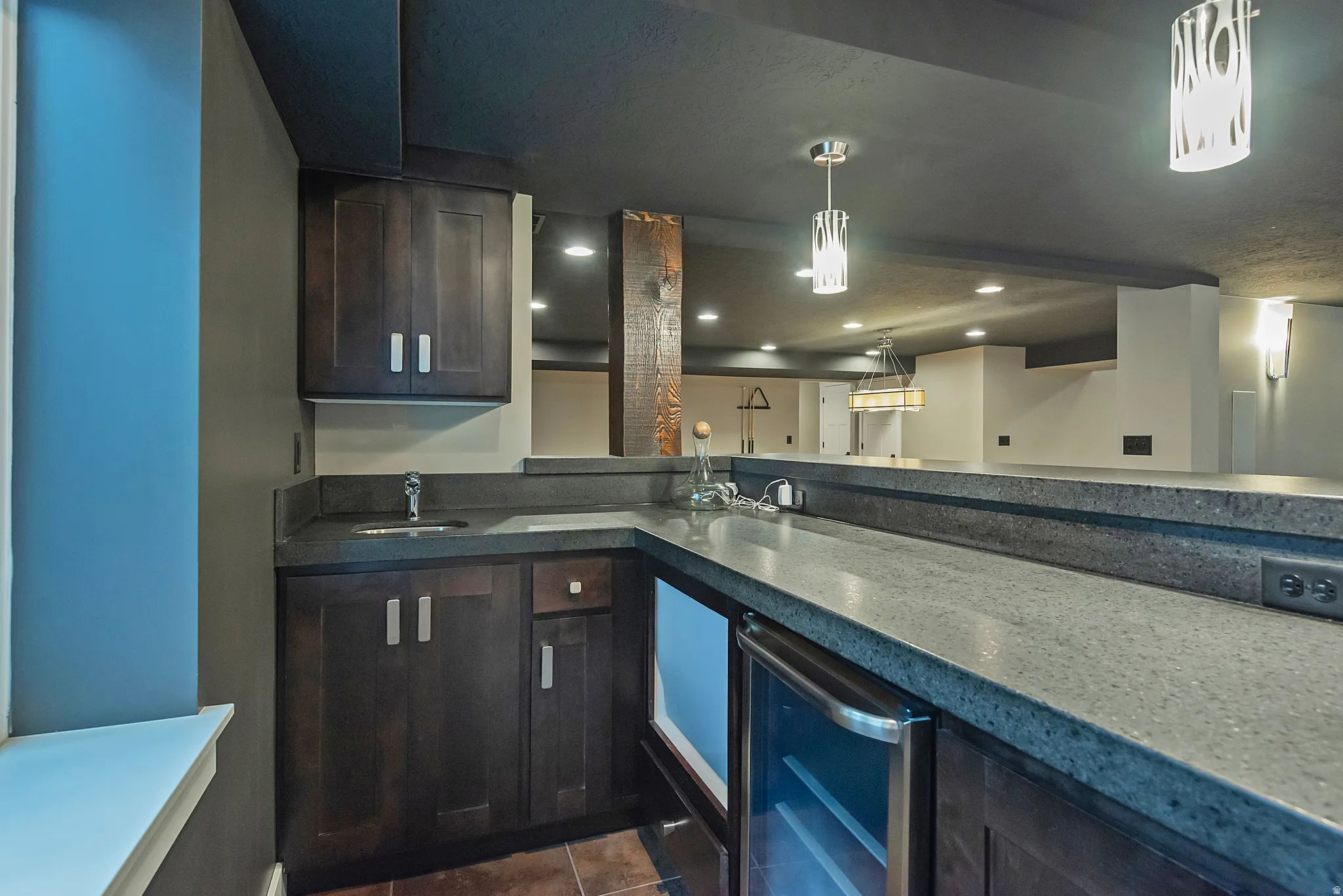 Modern kitchen featuring dark cabinetry with brushed metal hardware, quartz countertops with waterfall edge detail, stainless steel appliances, pendant lighting, and recessed ceiling lights