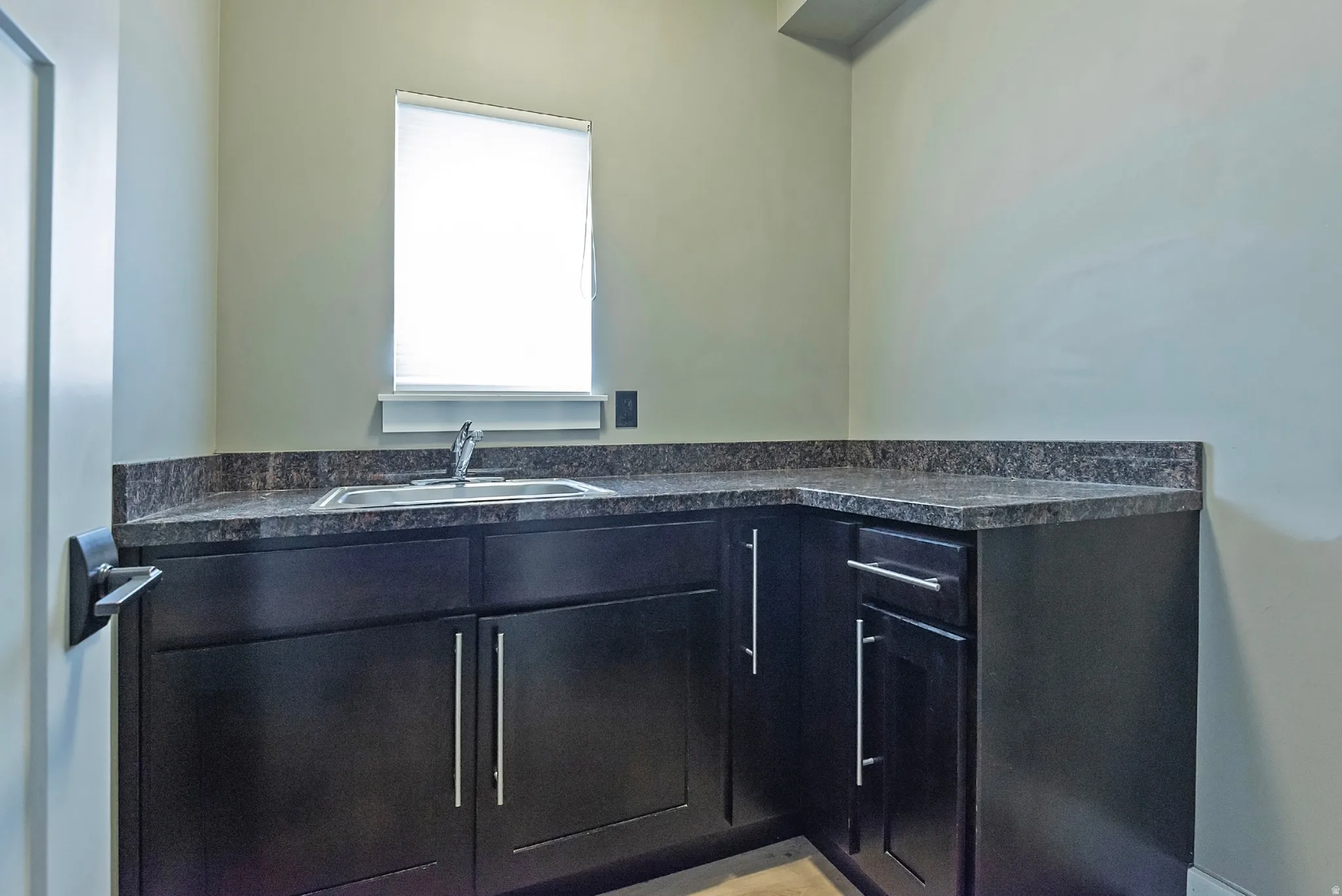 Modern bathroom vanity featuring sleek black cabinetry with chrome hardware, a gray stone countertop with an integrated sink, and a contemporary faucet