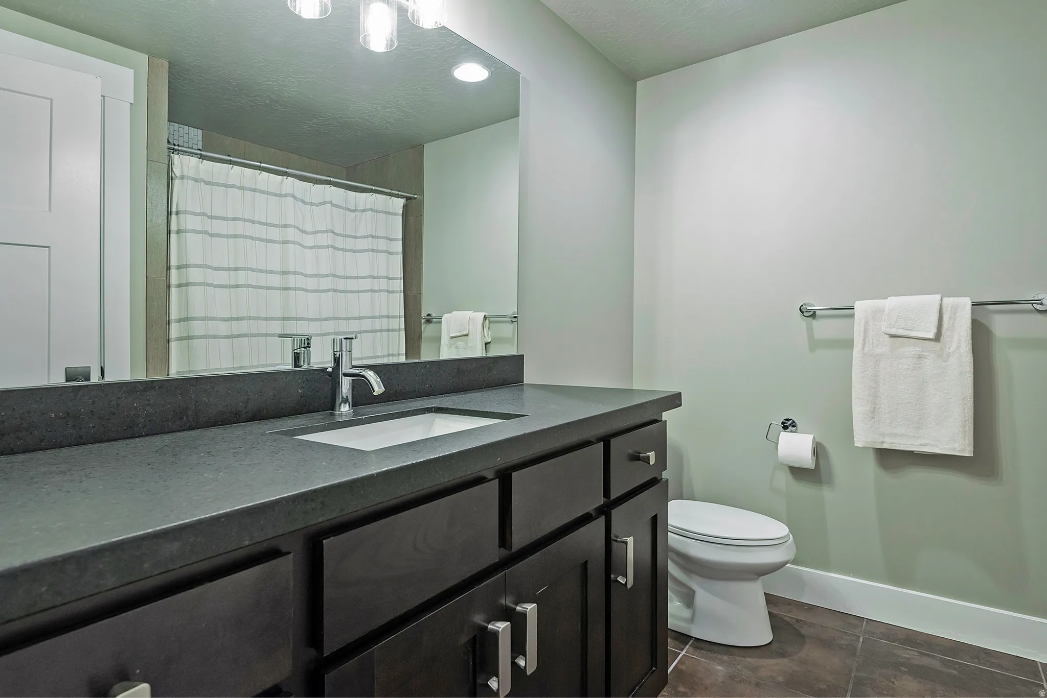 Modern bathroom featuring a dark wood vanity with dual-sink configuration, gray quartz countertop, recessed ceiling lighting, and chrome fixtures