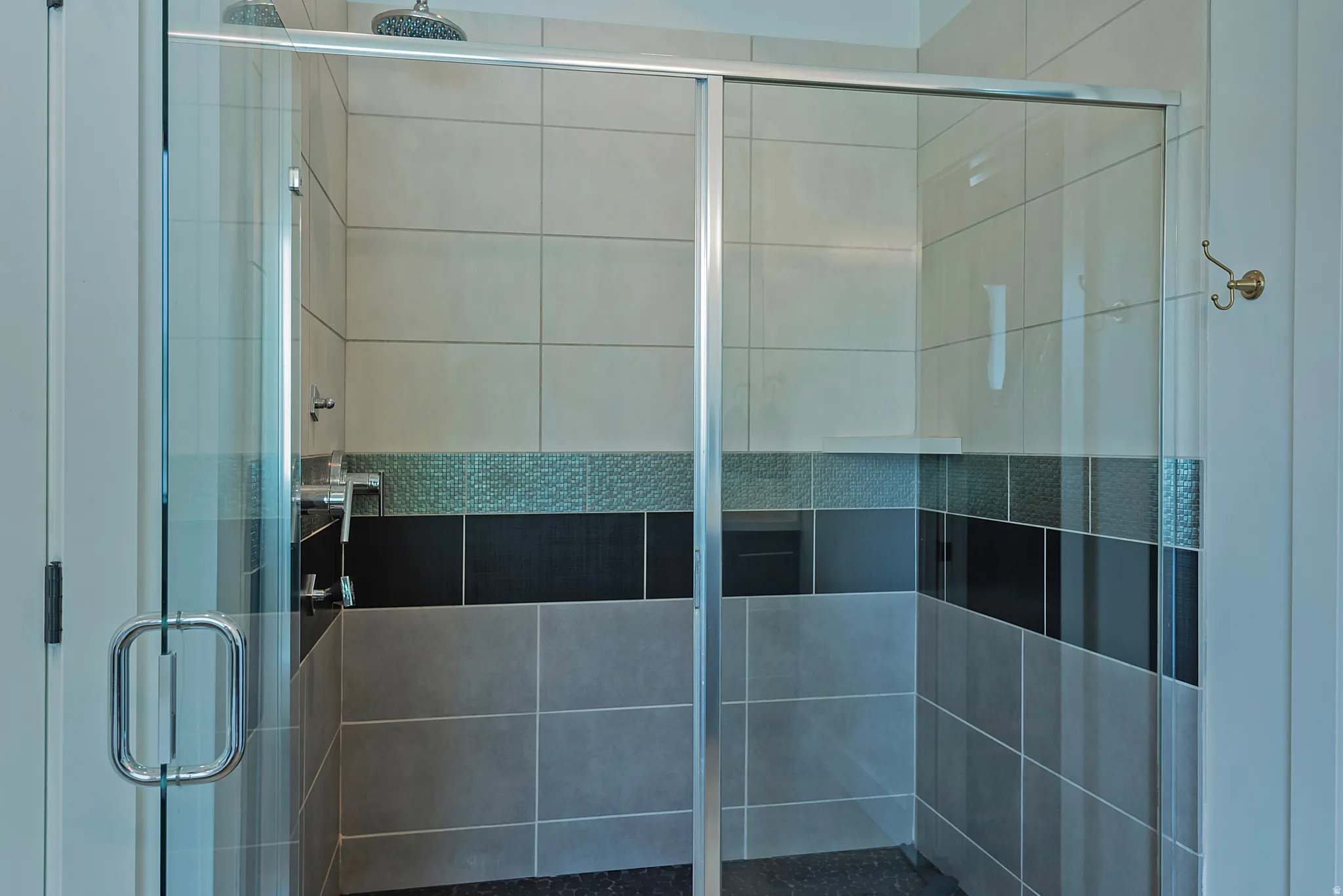 Glass-enclosed shower with a rainfall shower head, chrome fixtures, and a patterned tile accent band