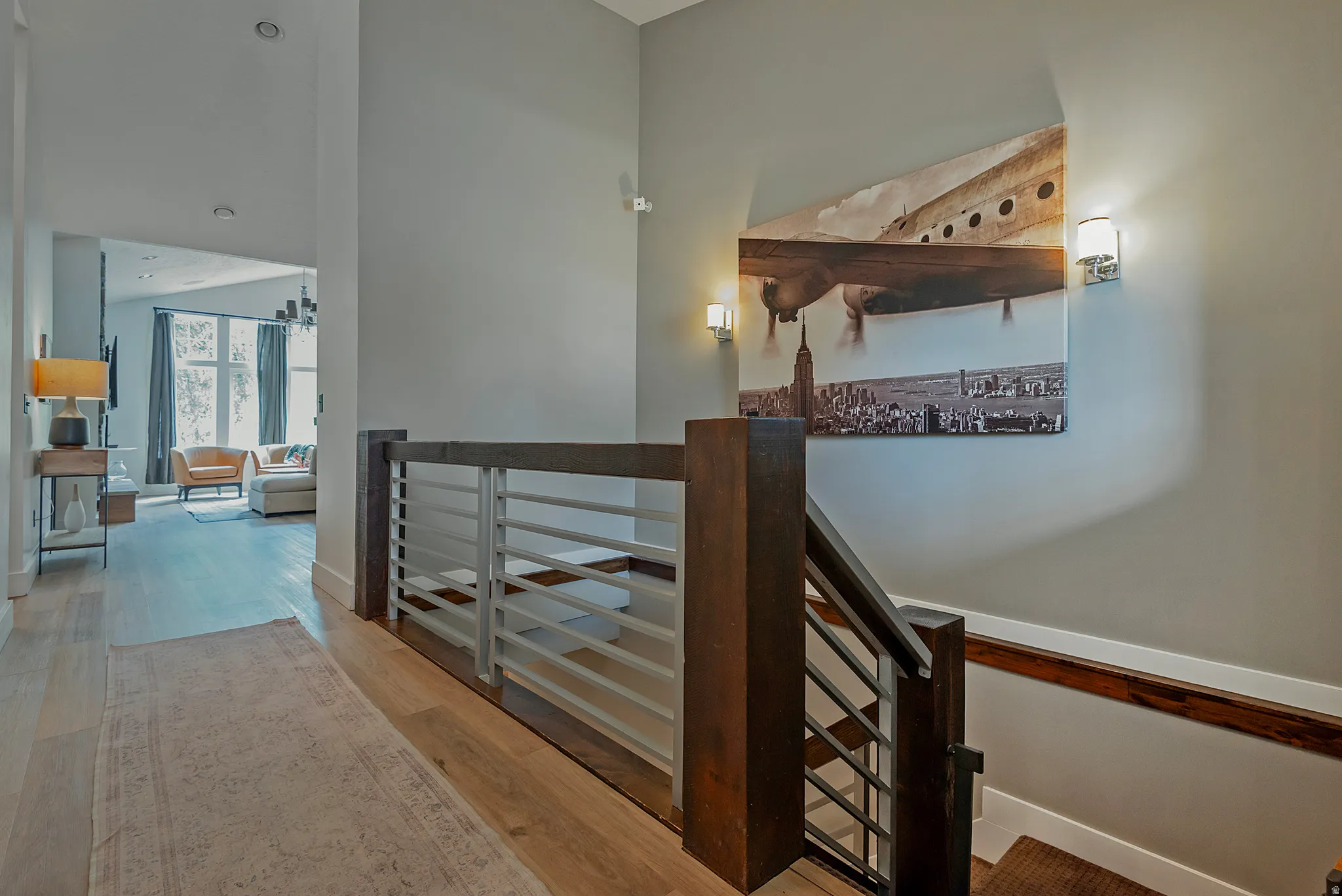 Modern hallway featuring a contemporary metal and wood railing system, warm wood-finish flooring, recessed ceiling lighting, and exposed wooden beam architectural detail