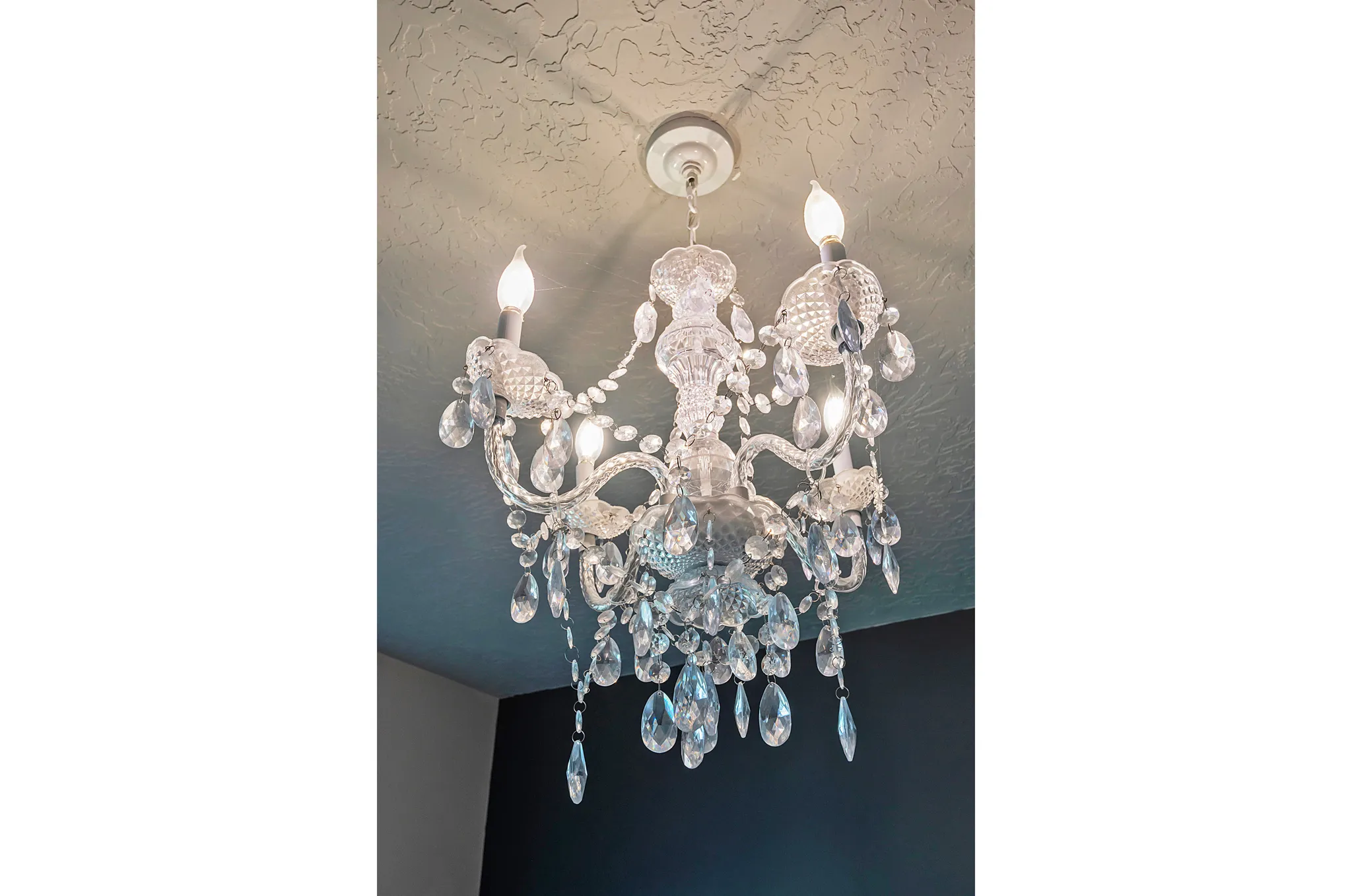 Elegant crystal chandelier with ornate scrollwork arms and cascading glass drops, featuring multiple candlestick-style light sources and a decorative ceiling medallion