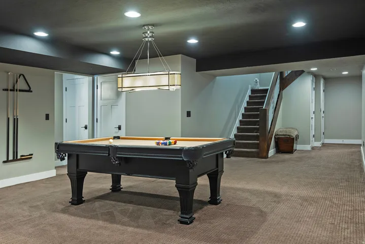 Finished basement recreation space featuring a professional-grade pool table with slate playing surface, recessed ceiling lighting with a coordinating pendant fixture, neutral carpeting throughout, and direct staircase access