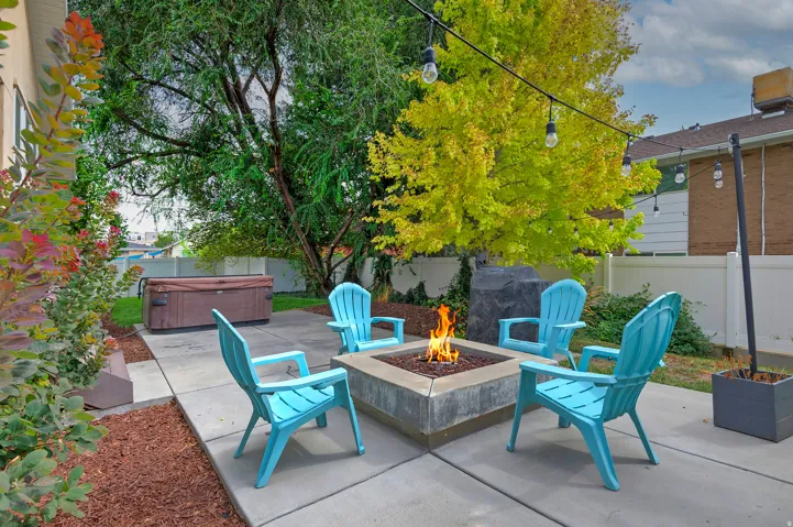 Backyard entertaining space featuring a built-in fire pit with stone surround, concrete patio, and mature shade trees