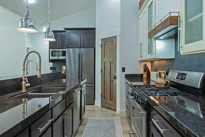 Stainless steel appliances, dark stone countertops, wood-finish flooring, recessed lighting, and a vaulted ceiling