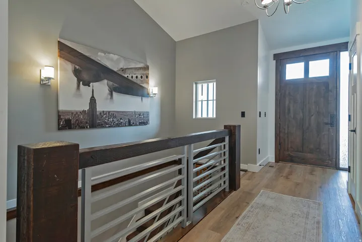 Wood-finish flooring, staircase with horizontal metal railings, dark wood newel posts, and a dark wood entry door with clear glass panels