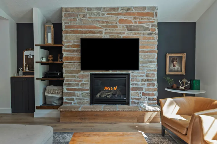 Striking focal point featuring a substantial brick fireplace with gas insert, mounted flat-screen television, and custom built-in shelving with dark cabinetry flanking either side