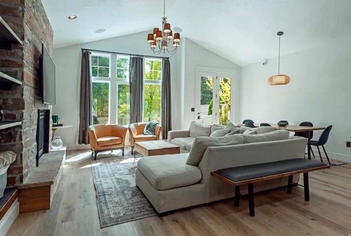 Expansive open-concept living space with soaring vaulted ceilings, large multi-pane windows flooding the room with natural light, and wide-plank wood-finish flooring throughout