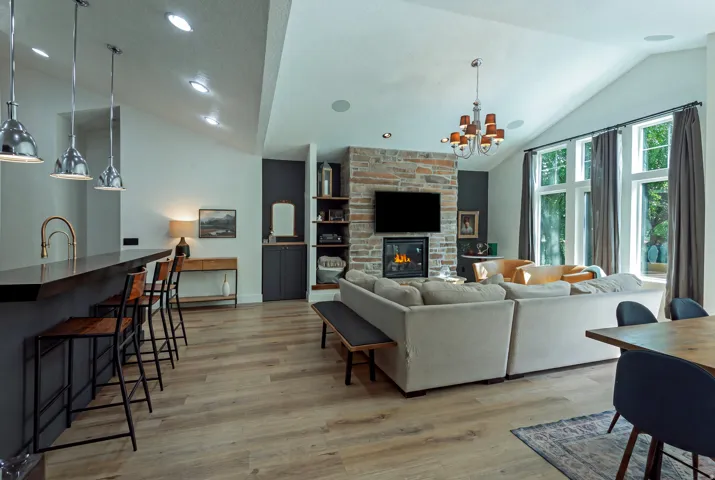 Vaulted ceiling with recessed lighting, stone-clad fireplace, wood-finish flooring, built-in shelving, and large windows