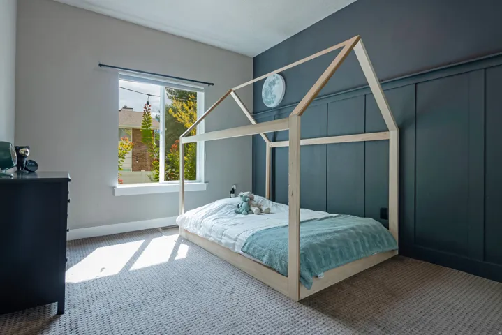 Bright bedroom featuring a wood-frame canopy bed, soft blue bedding, and natural light from a multi-pane window