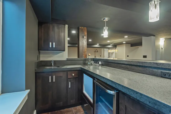 Modern kitchen featuring dark cabinetry with brushed metal hardware, quartz countertops with waterfall edge detail, stainless steel appliances, pendant lighting, and recessed ceiling lights