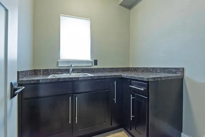 Modern bathroom vanity featuring sleek black cabinetry with chrome hardware, a gray stone countertop with an integrated sink, and a contemporary faucet