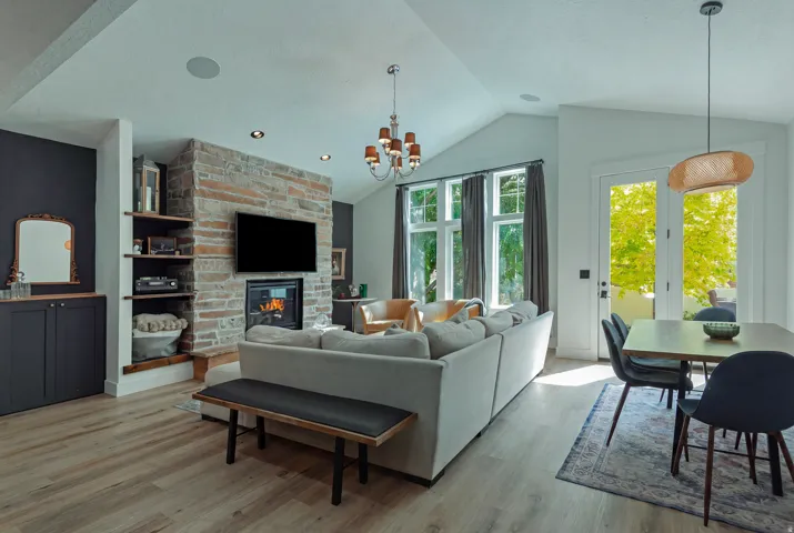Open-concept living space featuring a vaulted ceiling with recessed lighting, a gas fireplace with stacked stone surround and built-in shelving, and expansive glass doors and windows with natural light