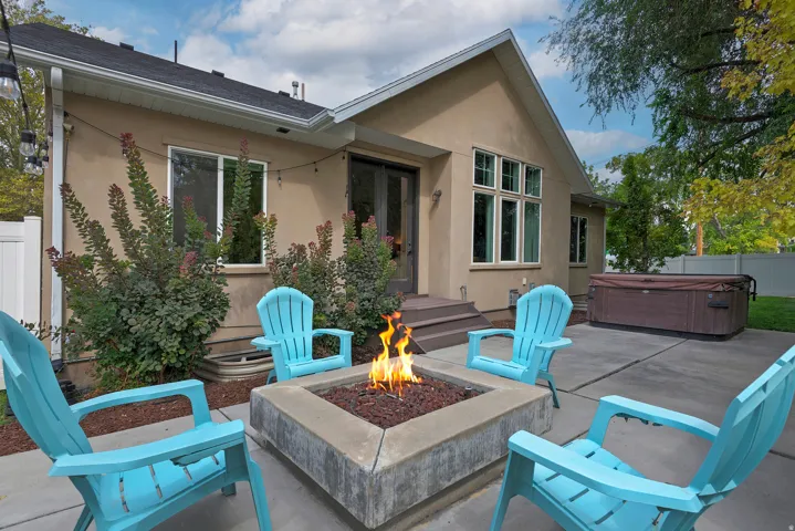 Modern backyard entertaining space featuring a built-in fire pit with stone surround, expansive paved patio, mature landscaping, and direct access to the residence
