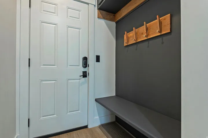 Modern entryway featuring a charcoal accent wall, wood-finish ceiling beam, and built-in wooden shelving