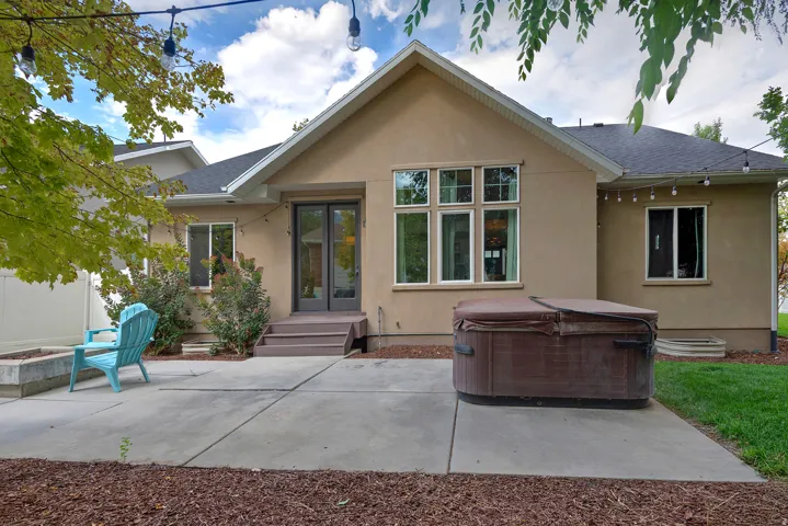 Contemporary home featuring a spacious poured concrete patio, mature landscaping with established trees, and a clean stucco exterior with a peaked roofline
