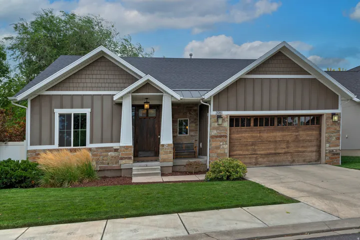 Contemporary ranch-style home featuring a stone and composite exterior, white trim detailing, and a two-car garage with wood-finish doors