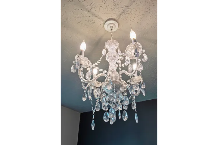 Elegant crystal chandelier with ornate scrollwork arms and cascading glass drops, featuring multiple candlestick-style light sources and a decorative ceiling medallion