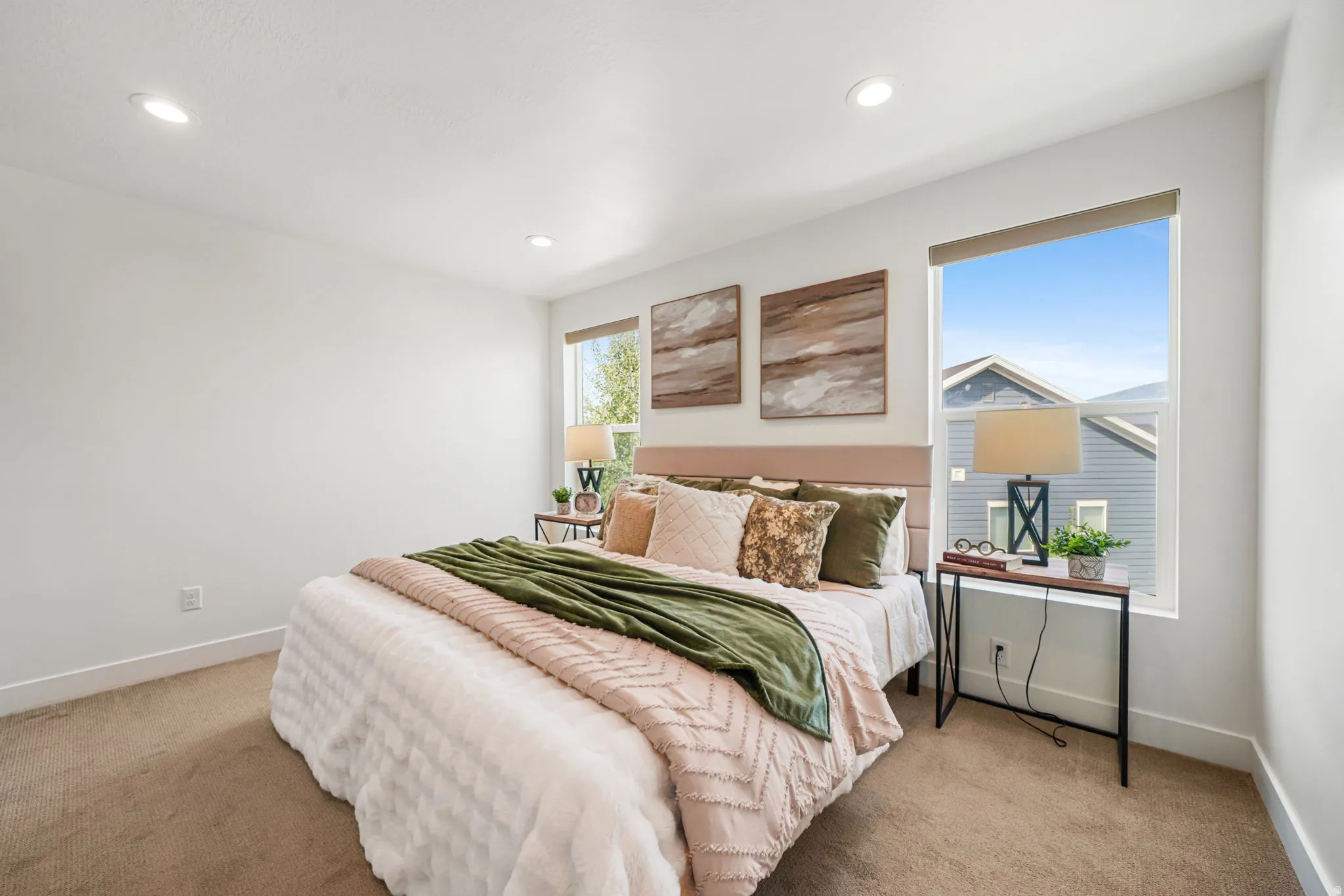 White walls with recessed lighting, two windows with roller shades, and neutral-toned carpeting